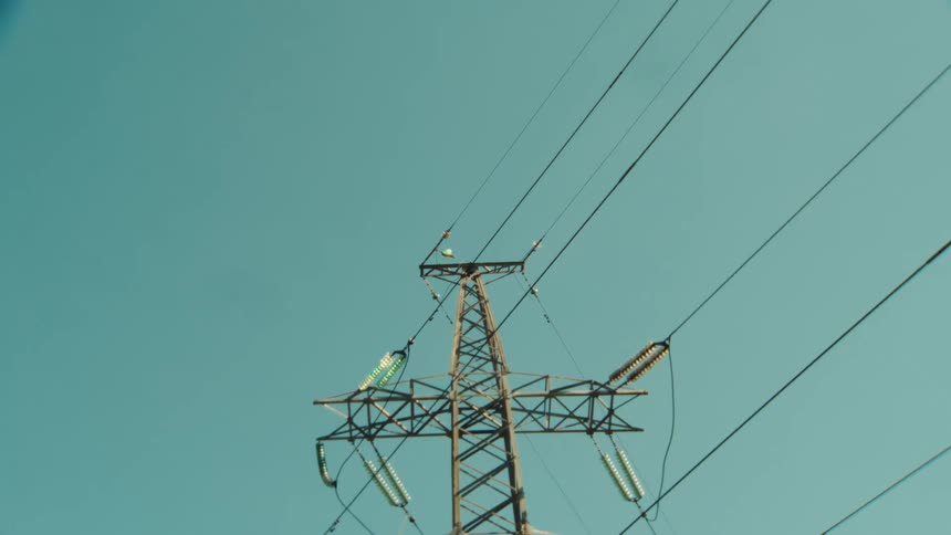 A yellow balloon is tragically tangled at the top of a high-voltage electrical tower as the camera slowly zooms out