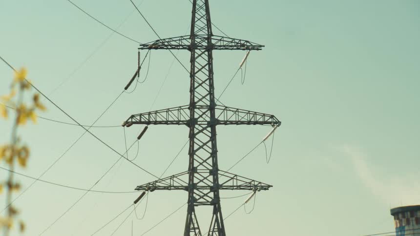 A slow zoom into a high-voltage electricity pylon at an industrial power plant on a sunny day