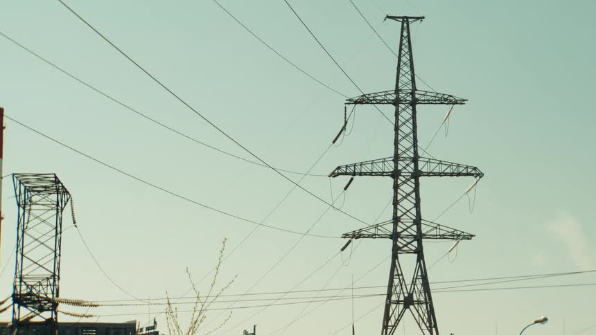 A slow zoom focuses on a massive high-voltage electricity pylon standing amidst the infrastructure of a power plant