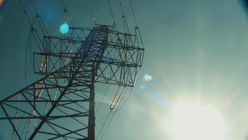 Slow tilt-up shot of a high-voltage electricity pylon against a sun-drenched clear sky