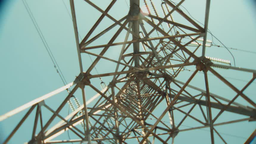 Looking up through the intricate metal lattice of a high-voltage transmission tower against a clear blue sky
