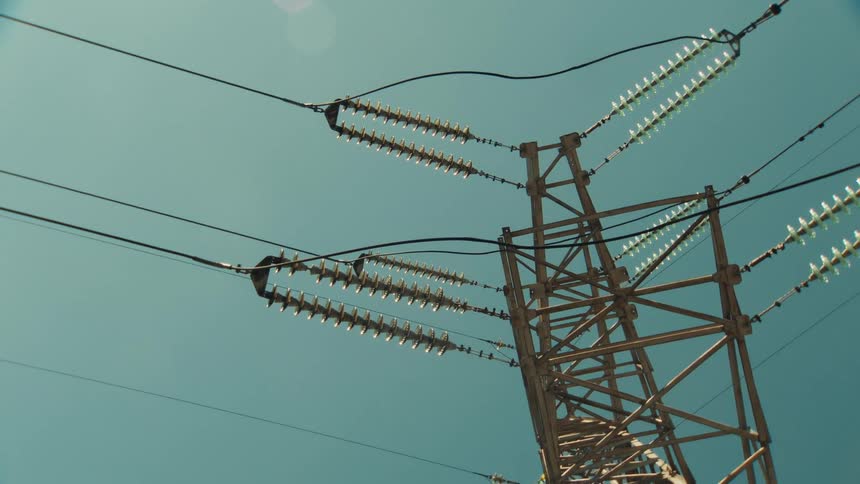A close-up low-angle view of a high-voltage electricity pylon with power lines against a clear blue sky