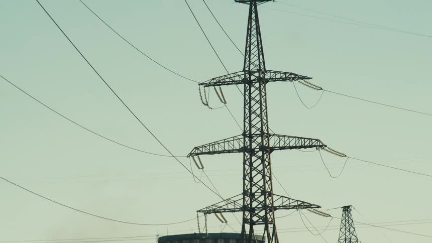 A slow zoom out from a high-voltage electricity pylon reveals a large thermal power plant with its cooling towers and surrounding industrial area