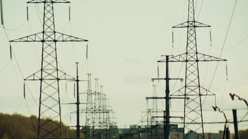 Rows of electricity transmission towers stand against a hazy sky, shimmering in the heat