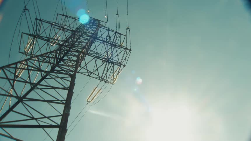 An upward-looking slow zoom reveals a high-voltage electricity transmission tower against the sun