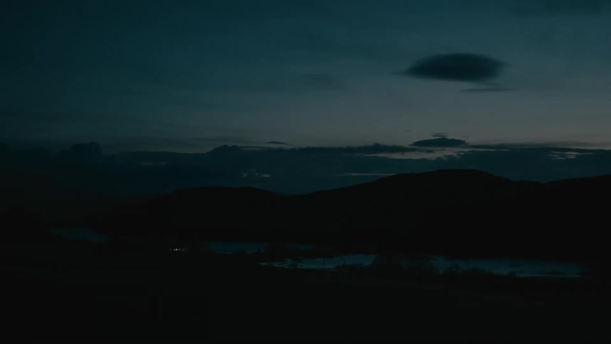 A serene landscape of silhouetted mountains and a reflective lake under a deep blue twilight sky