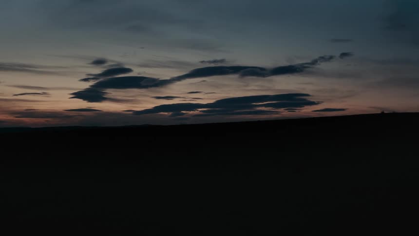 Unique dark cloud formations float in a colorful twilight sky over a silhouetted landscape