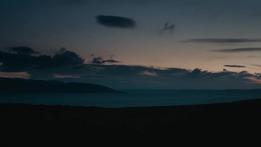 A serene wide shot of a tranquil sea during twilight with silhouetted mountains in the distance