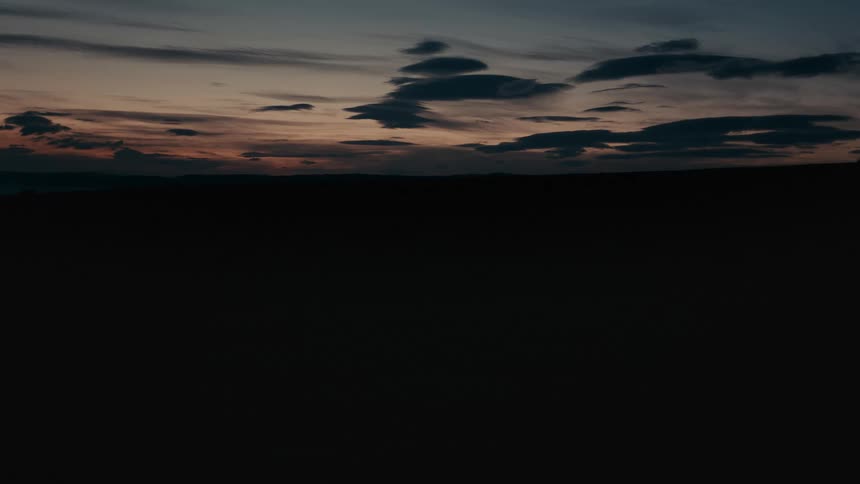 A static wide shot captures the dramatic, colorful sky at twilight over a dark, silhouetted desert landscape