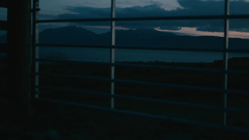 A still, moody shot of a mountain loch at twilight, viewed from behind a farm gate