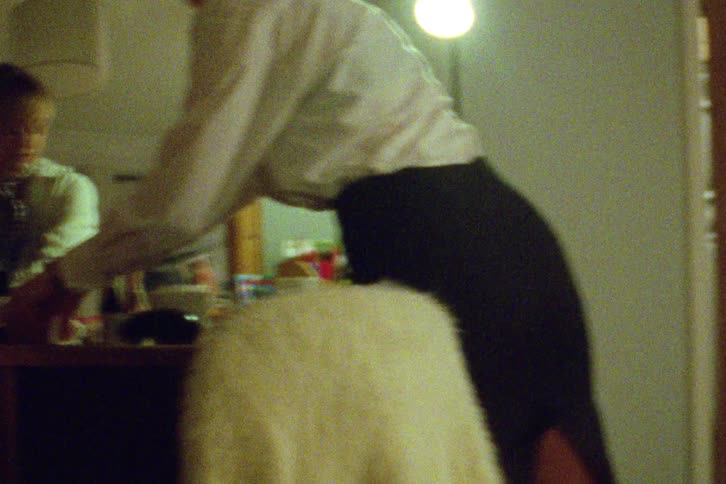 A woman packs her vintage suitcase in a dimly lit bedroom, captured on grainy film