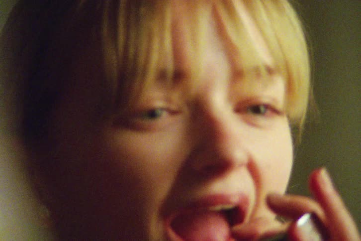 Introspective close-up shot on vintage film of a young woman applying lipstick