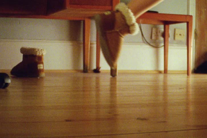 A low-angle view shows a person's fidgety feet, one bare and one in a fuzzy boot, tapping on a shiny wooden floor