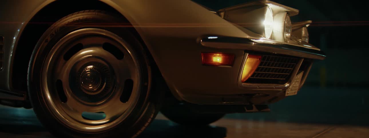 The front tire and illuminated headlight of a vintage Corvette Stingray are shown in a stylish close-up