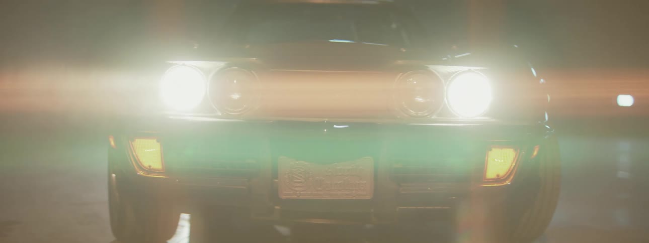 Bright headlights on a classic sports car turn on in the darkness, creating a cinematic lens flare