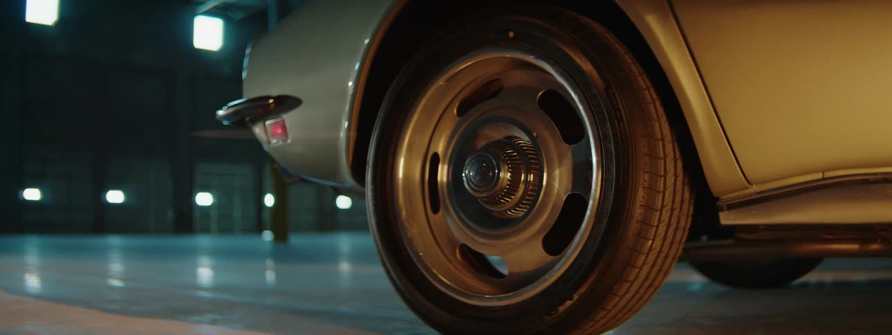 Cinematic close-up of a vintage car's shiny wheel rim and tire parked inside a dark garage