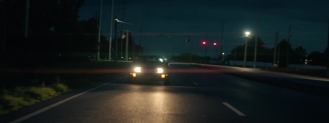 Moody shot of a dark car idling at a red light on a suburban street at night with a lens flare