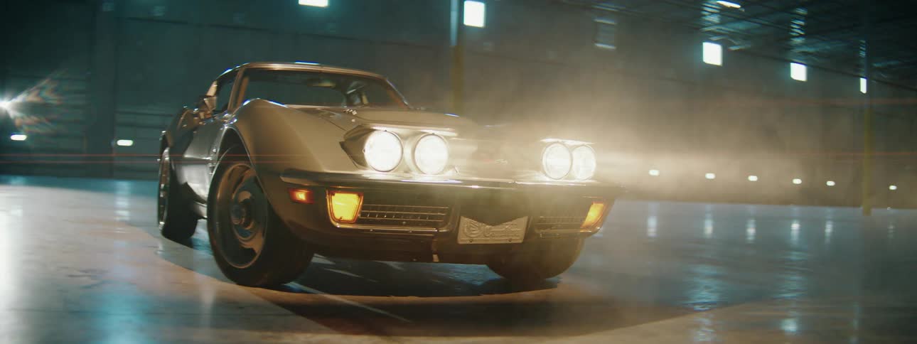 Cinematic shot of a vintage silver sports car with bright headlights glowing through smoke in a dark warehouse