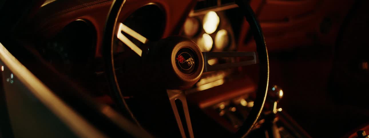 A static close-up shot of a classic Corvette steering wheel in a warmly lit, nostalgic interior