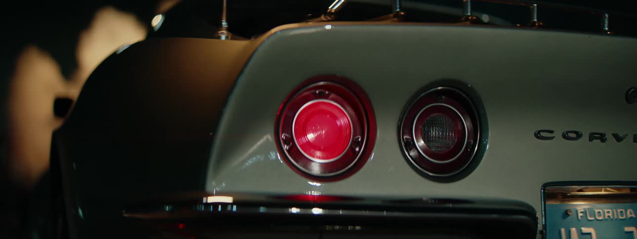 The glowing red taillight of a classic silver sports car is detailed in a dramatic close-up shot