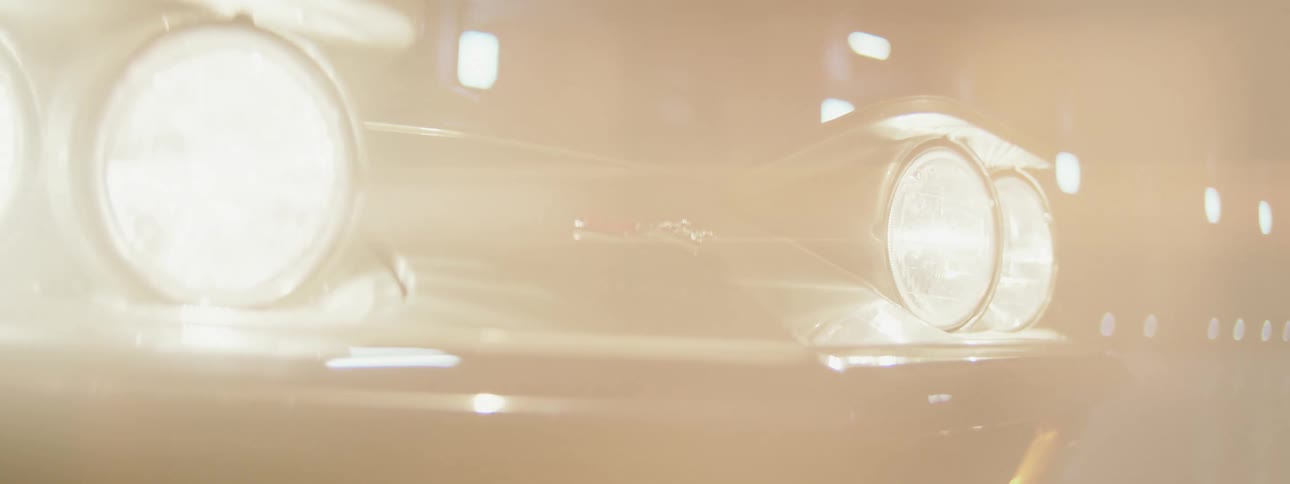 Bright headlights on a classic black sports car illuminate a smoky tunnel, with the lens flare eventually washing out the entire frame