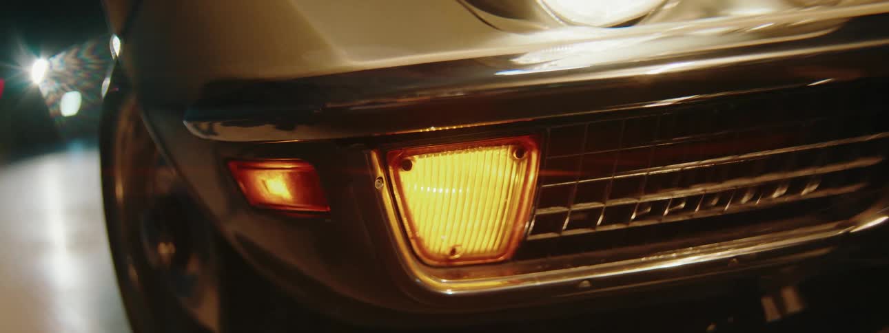 A shaky close-up shot captures the glowing yellow headlight of a vintage car