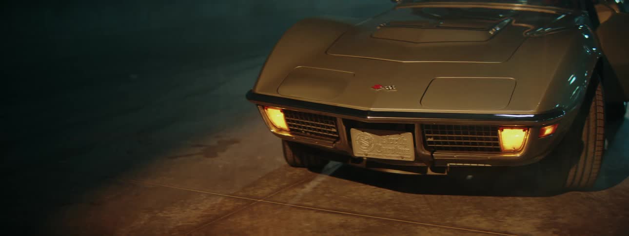 A classic silver car's turn signals blink on and off in a dimly lit, moody setting