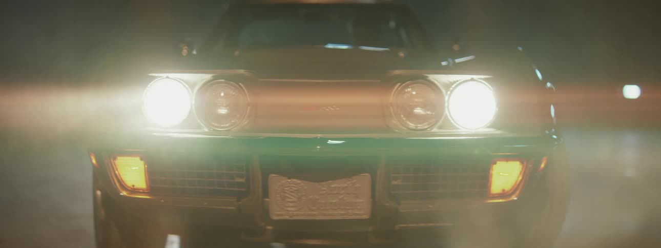 Headlights on a vintage green Corvette Stingray shine brightly in a dark, moody setting