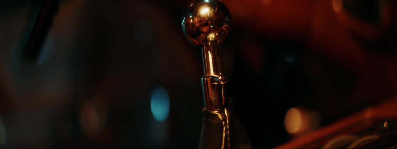 A slow tilt up on the chrome gear stick of a vintage car at night with warm, moody lighting