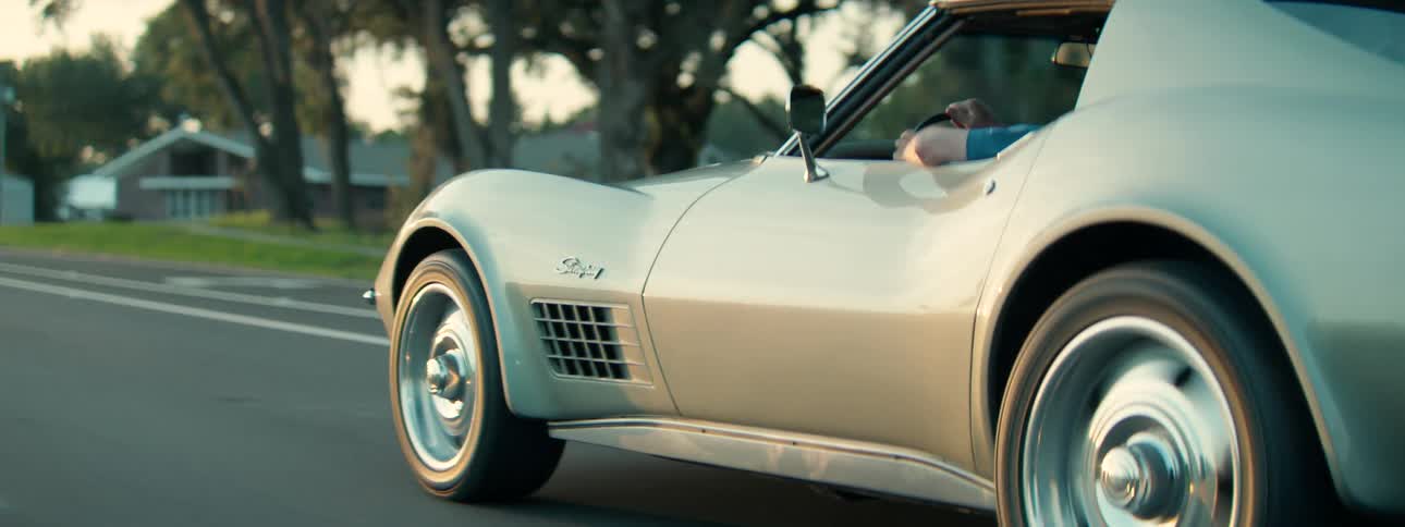 Close-up tracking shot of a classic American sports car driving on a road in the warm evening light