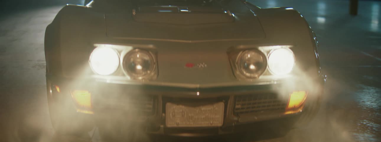 A classic sports car's bright headlights cut through the smoke in a dark, mysterious setting at night