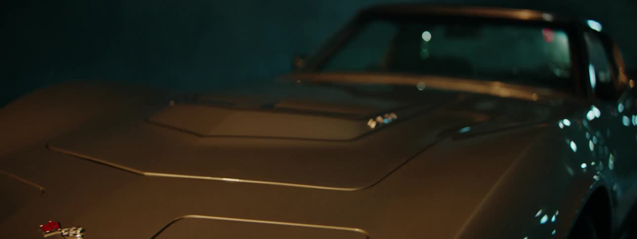 A close-up shot slowly reveals the front hood of a classic silver Corvette Stingray at night