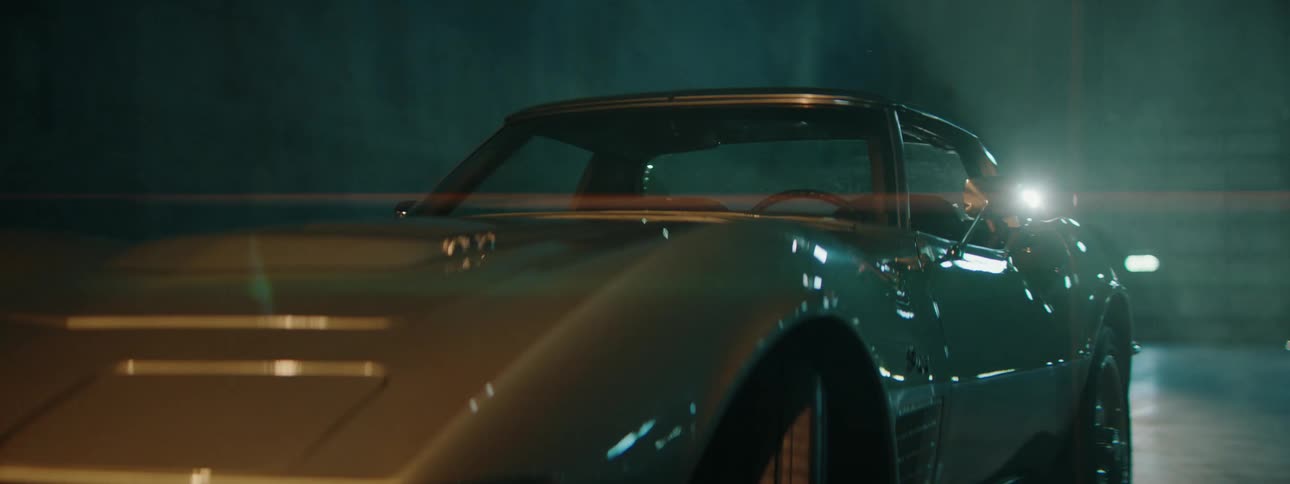 A sleek, vintage silver sports car is revealed in a slow, cinematic pan within a dark and smoky garage