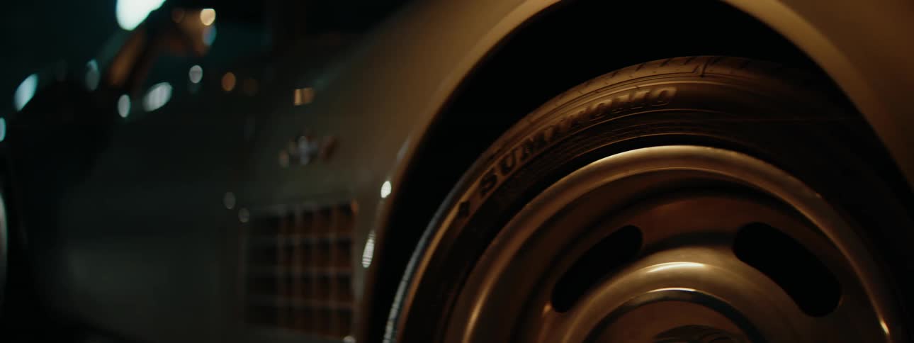 A moody, cinematic close-up of a classic sports car's spinning wheel and tire reveals the iconic Stingray emblem