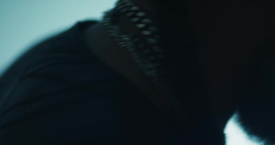 A moody, silhouetted extreme close-up of a man wearing multiple silver chains around his neck
