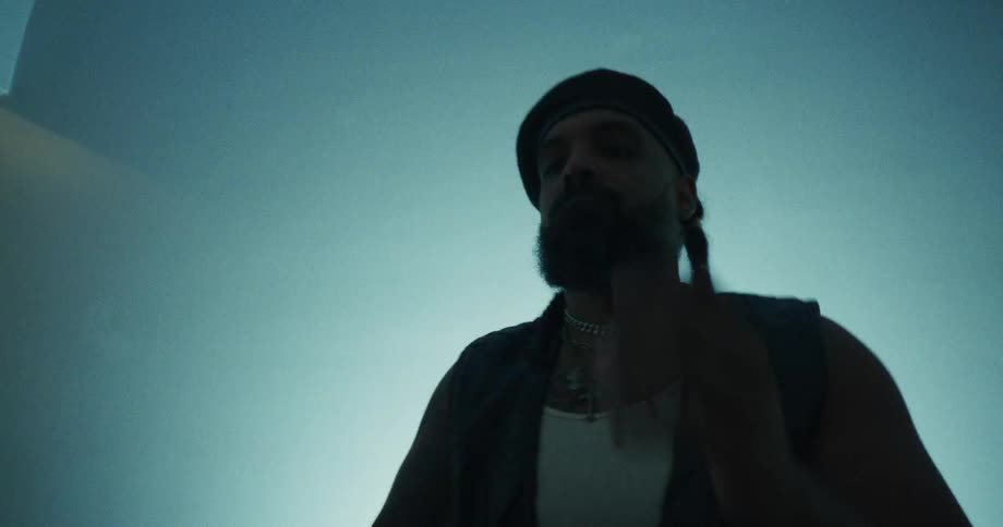 Slow motion, low-angle shot of a male musician playing a hand drum in a dark, atmospheric setting