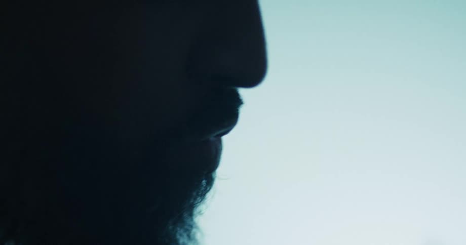 A dramatic and moody close-up silhouette of a bearded man's profile against a cool-toned background