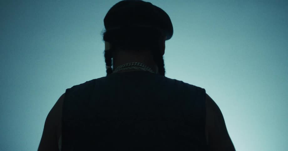 From behind, a man in a beret is silhouetted against a blue background as he dances in slow motion