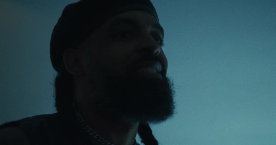 Low angle close up of a charismatic man with a beard and beret smiling in a dark, moody blue room