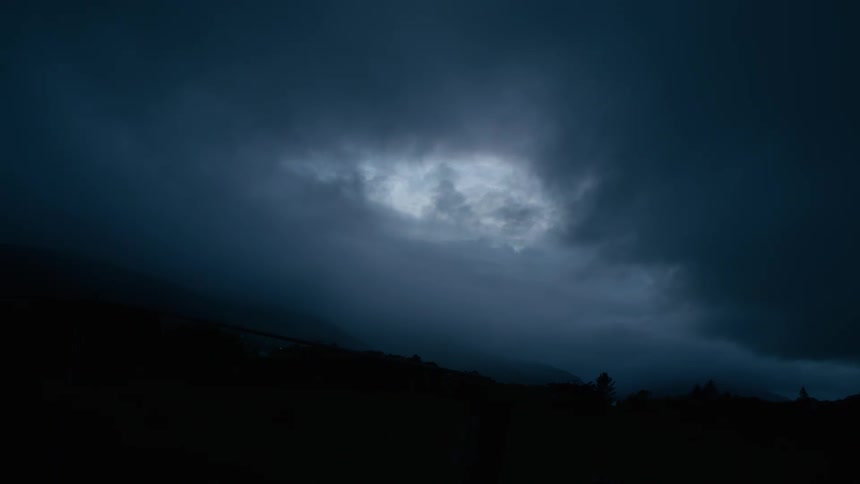 A single patch of moonlight illuminates the dark, stormy clouds gathering in the night sky