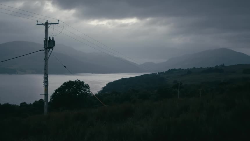 A utility pole stands watch over a remote, misty lake and mountains under a dark and moody overcast sky