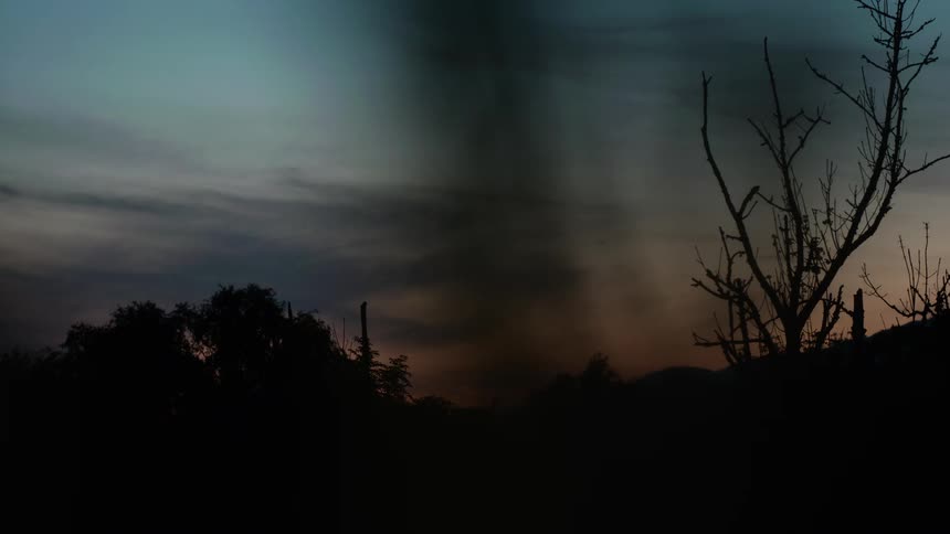 A dark, swirling tornado forms over a silhouetted landscape under a dramatic twilight sky