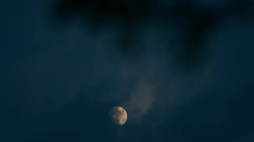 A mysterious moon glows in the dark night sky, partially obscured by slow-moving clouds and framed by dark tree leaves