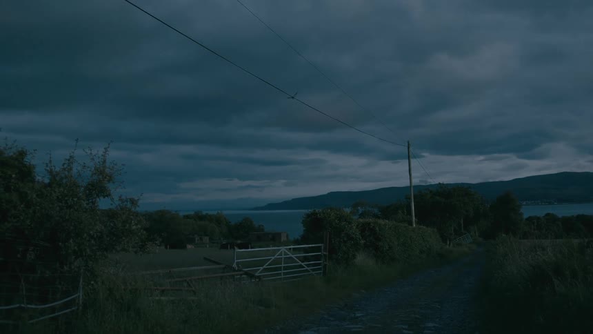A moody rural landscape with a dirt road leading to a lake at dusk under a stormy sky