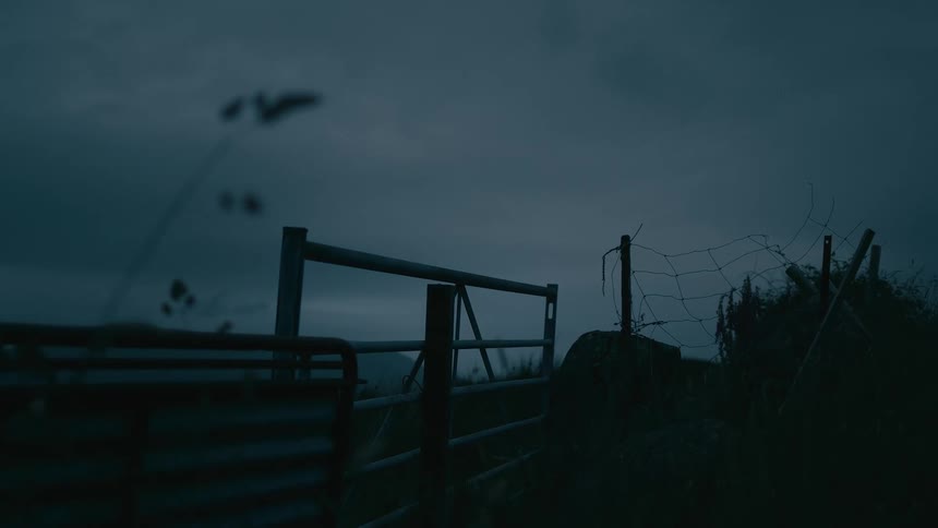A desolate farm gate is silhouetted against a dark and moody sky at dusk