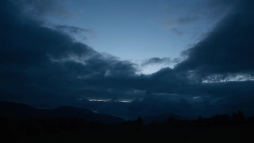 Dark, moody clouds gather over a mountain range silhouette during a serene twilight