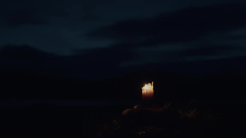 A lit candle with a flickering flame provides a single point of light in the darkness