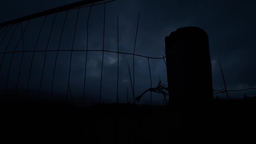 A dark and ominous silhouette of a fence and post against a cloudy night sky