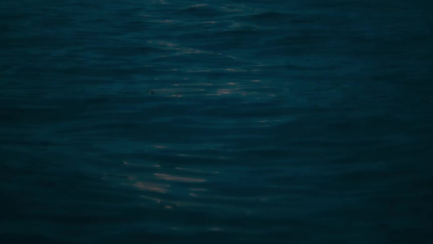 A close-up, moody shot of dark teal ocean water gently rippling at dusk