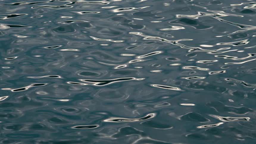 A relaxing close-up shot of gentle, dark blue water ripples with shimmering light reflections